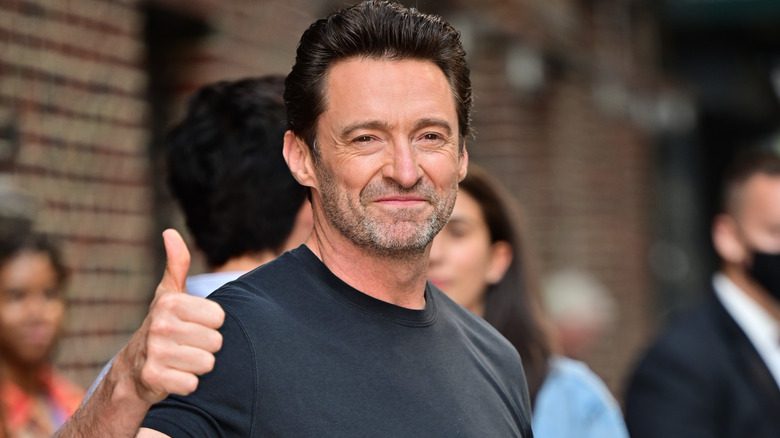 Hugh Jackman en chemise noire, souriant et faisant un pouce levé