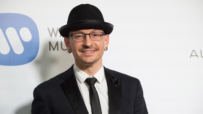 Chester Bennington souriant avec un chapeau noir et un costume