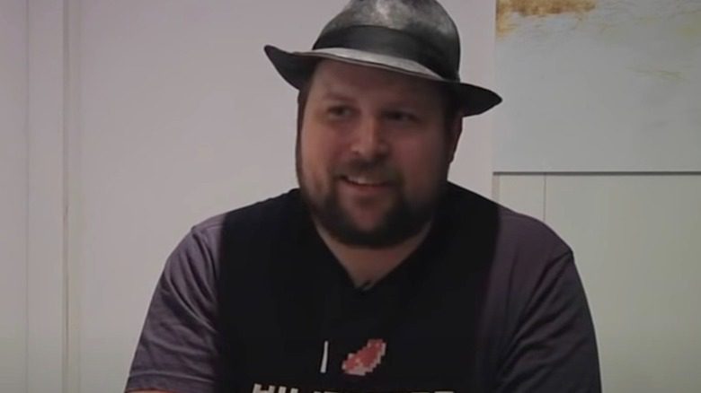 Markus Persson en chapeau fedora avec un sourire en coin